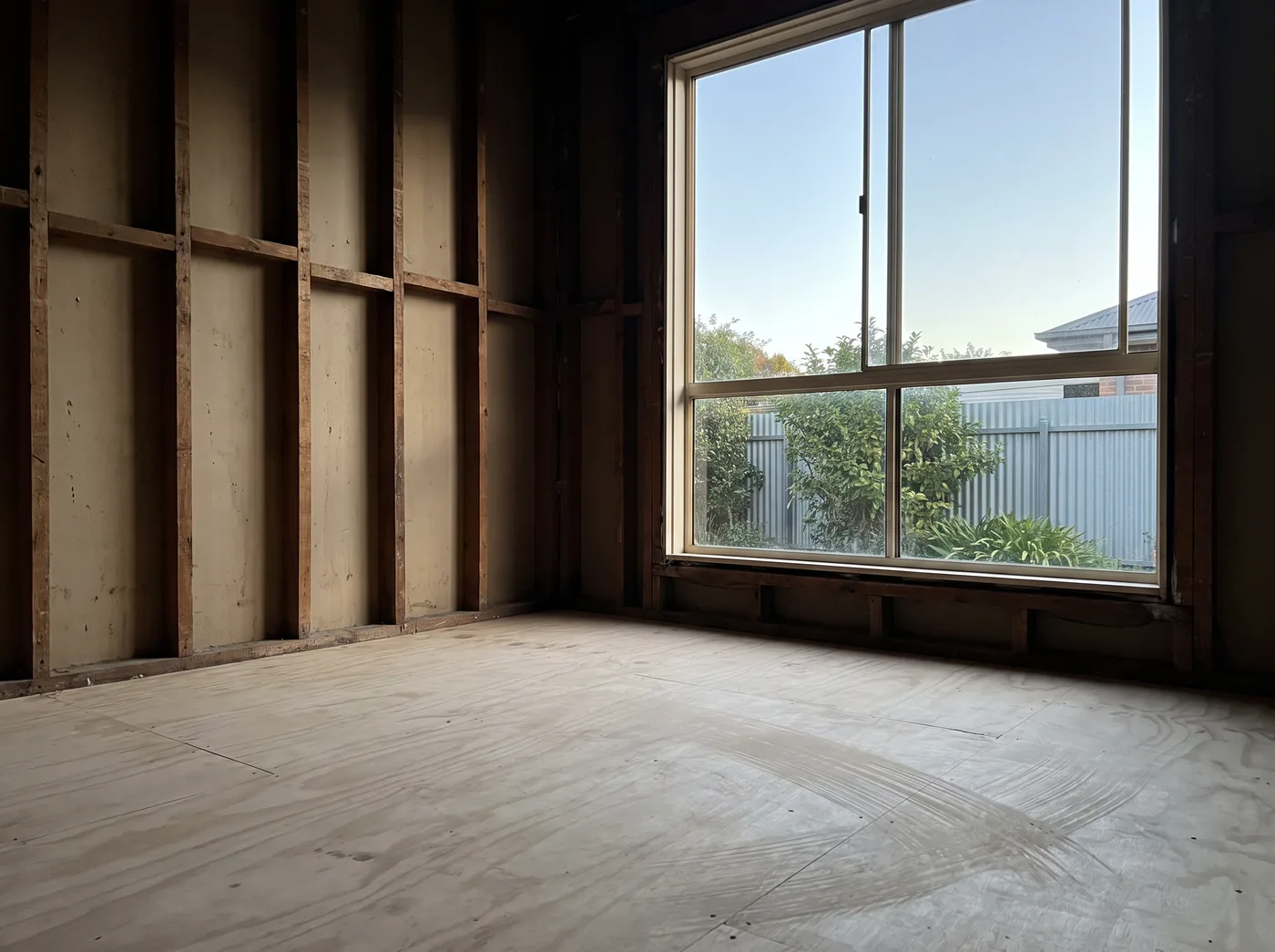 A renovation room with bare stud framing and a broom-swept plywood subfloor, cleared of all debris and ready for the next trade